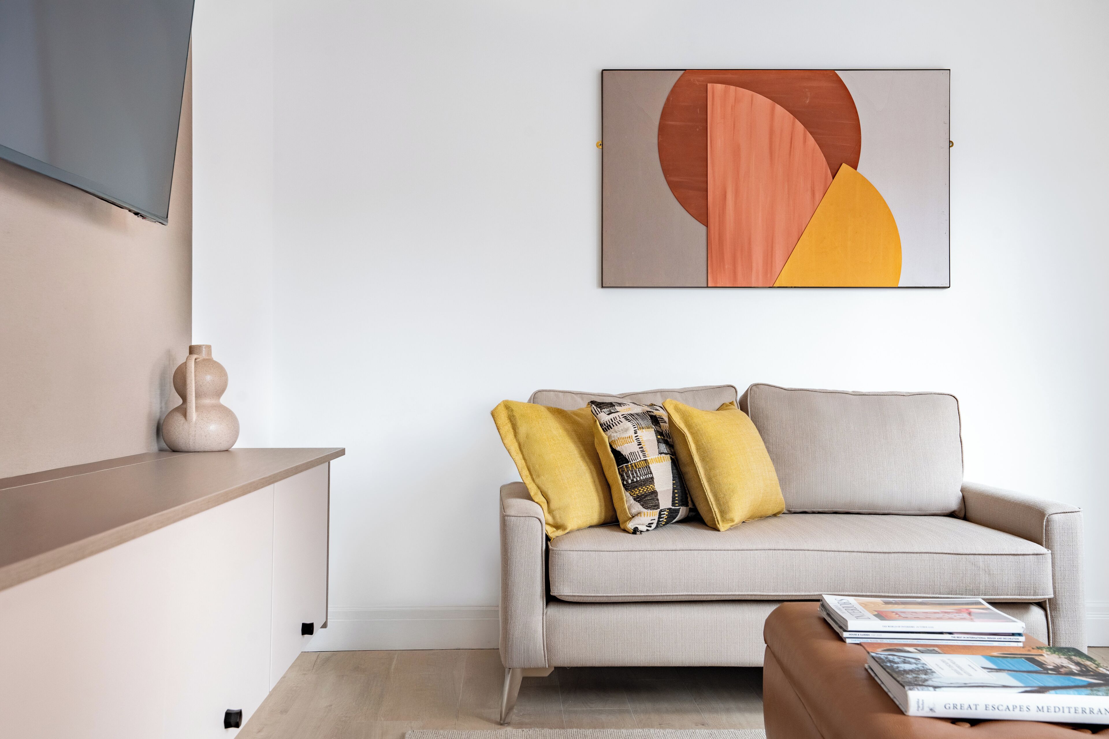 Un salon moderne avec un canapé, des coussins, un téléviseur à écran plat et un tableau.