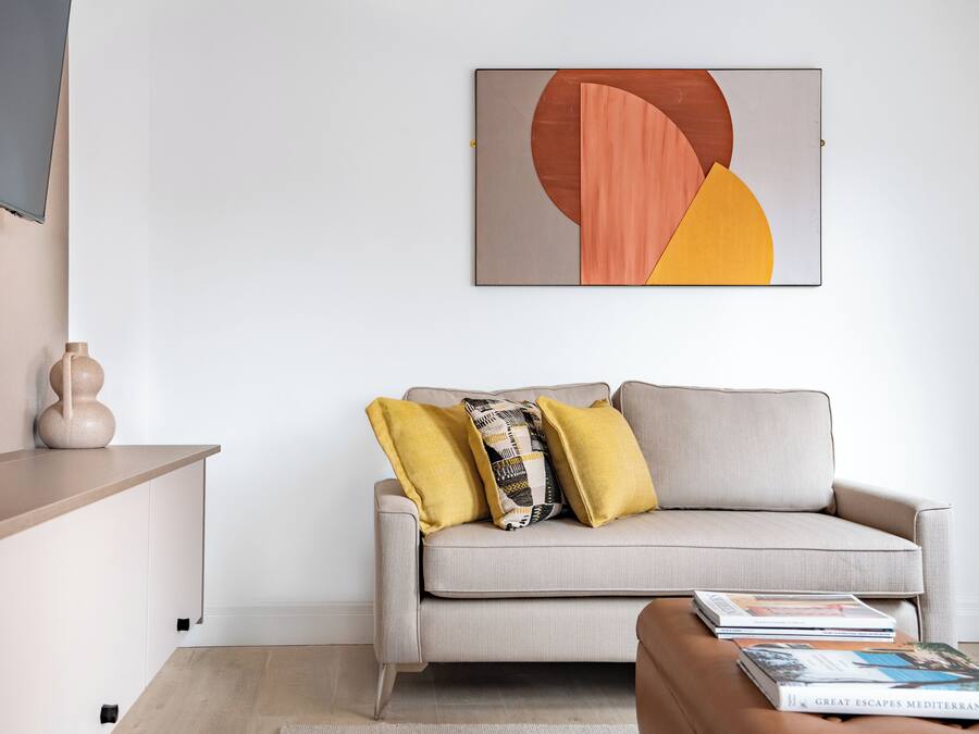 A modern living room with a sofa, cushions, a flat-screen TV, and a painting.