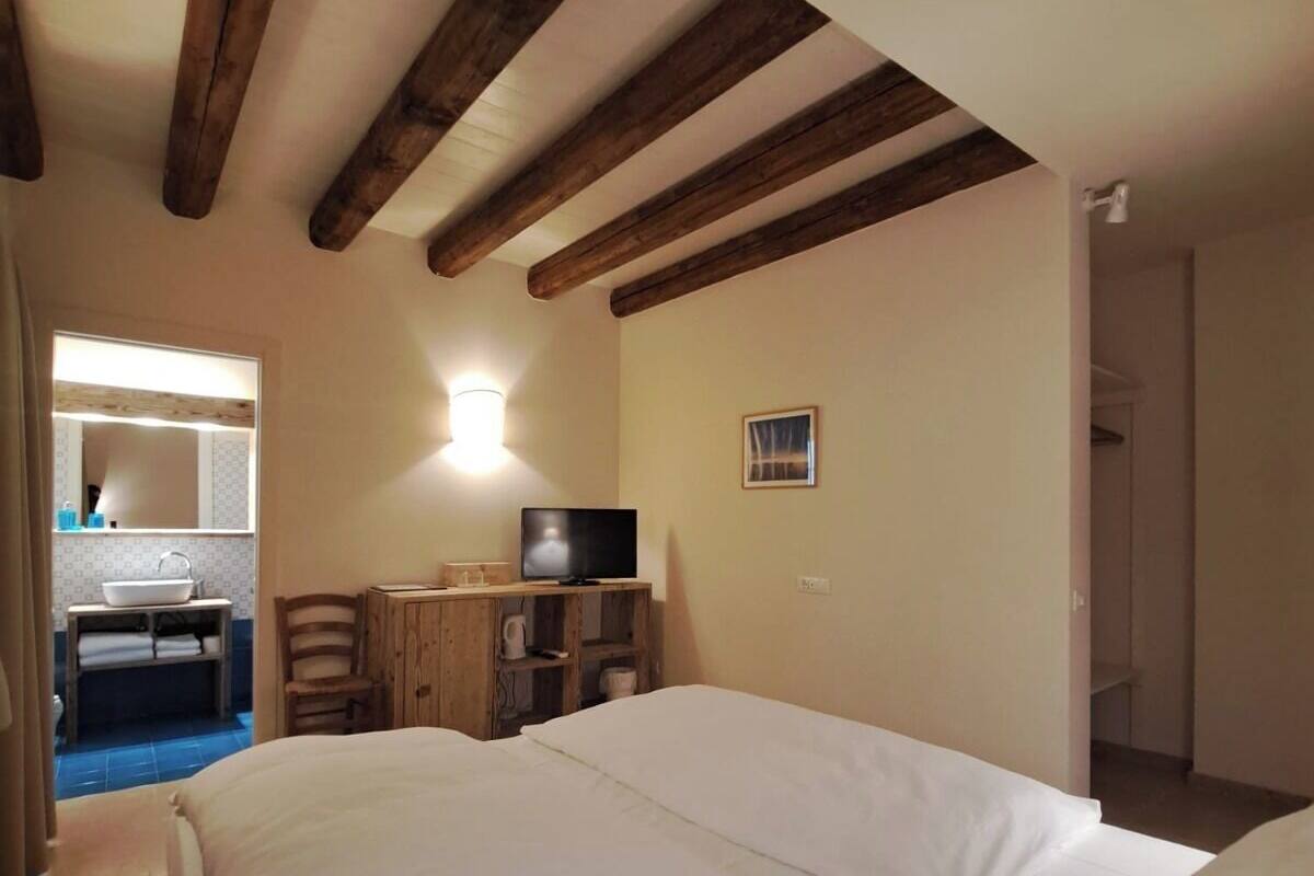 Ein Schlafzimmer mit einem großen Bett, Holzbalken an der Decke, einem Fernseher auf einem Holzboden und einem kleinen Tisch mit einem Stuhl.
