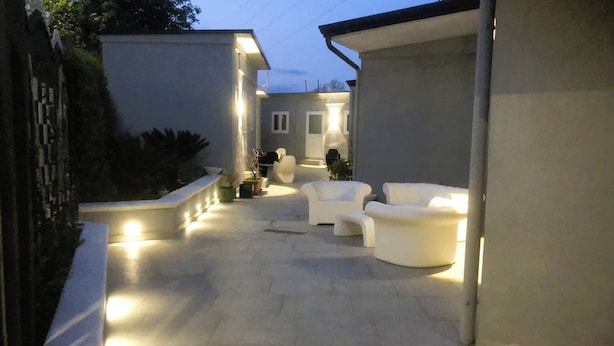 An outdoor patio area with white sofas and a stone floor, surrounded by walls and potted plants. - HOTEL SERENA (Naples)