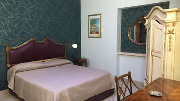 A bedroom with a bed, a wooden table, a chair, a dresser, and a wall-mounted mirror.