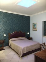 Een slaapkamer met een bed, nachtkastje, stoel, klein tafeltje en een wandlamp.