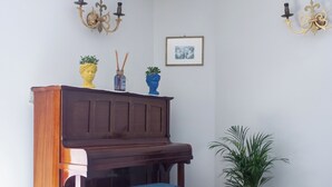 A piano with a bench, a potted plant, and wall-mounted decorations. - HOTEL SERENA (Naples)
