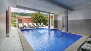 A modern indoor swimming pool with clear blue water, surrounded by lounge chairs and a view of a mountain landscape. - Villa Oliva Vilea in Sveta Marina  - Haus für 8 Personen (Labin)