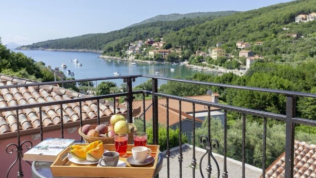 A balcony with a tray of food and drinks, overlooking a coastal town with boats on the water and houses on the hillside. - Villa Oliva Vilea in Sveta Marina  - Haus für 8 Personen (Labin)