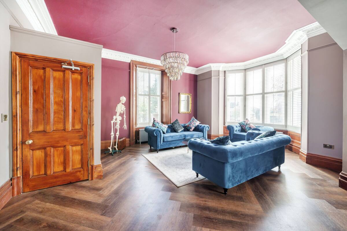 Une pièce avec une porte en bois, un canapé bleu, un lustre et de grandes fenêtres.