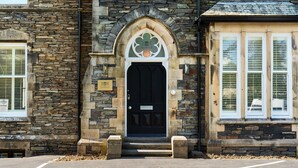 A stone building with a black door, a green emblem, and a plaque. - The Governance Apartments (Windermere)