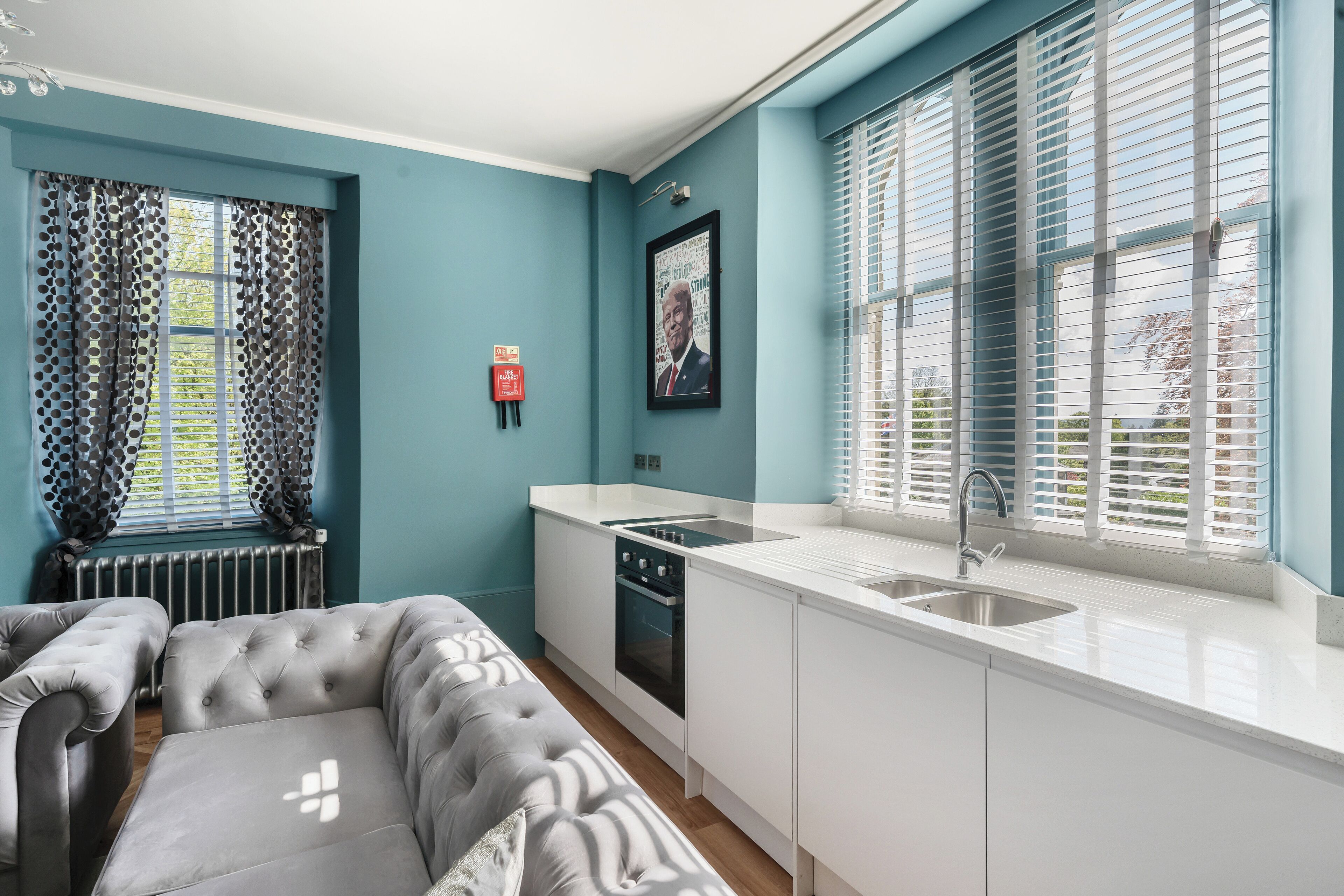 A compact kitchen with a built-in oven, a sink, and a window with blinds.