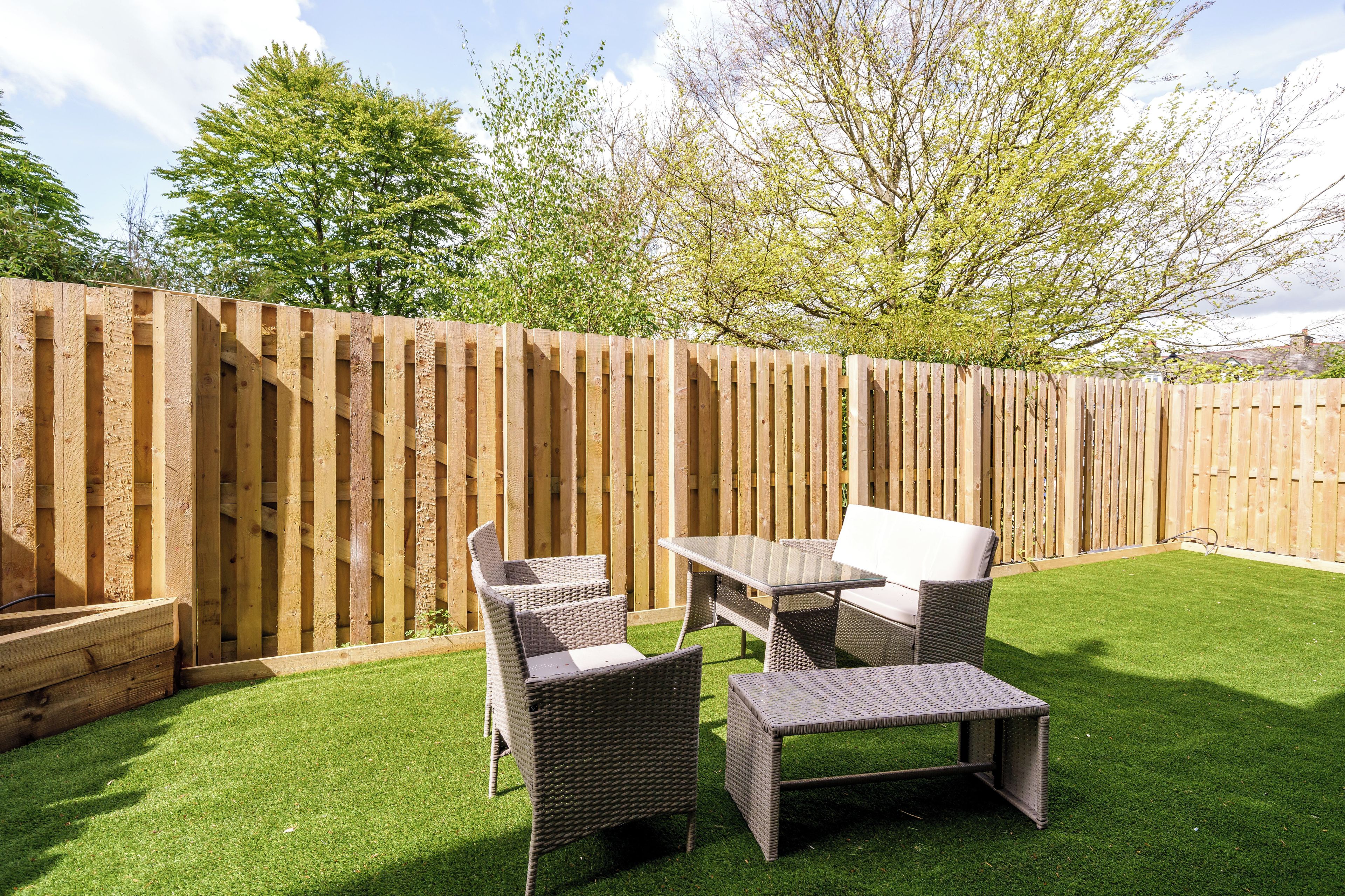 A backyard with a wooden fence, a grassy lawn, and outdoor furniture including a table and chairs.