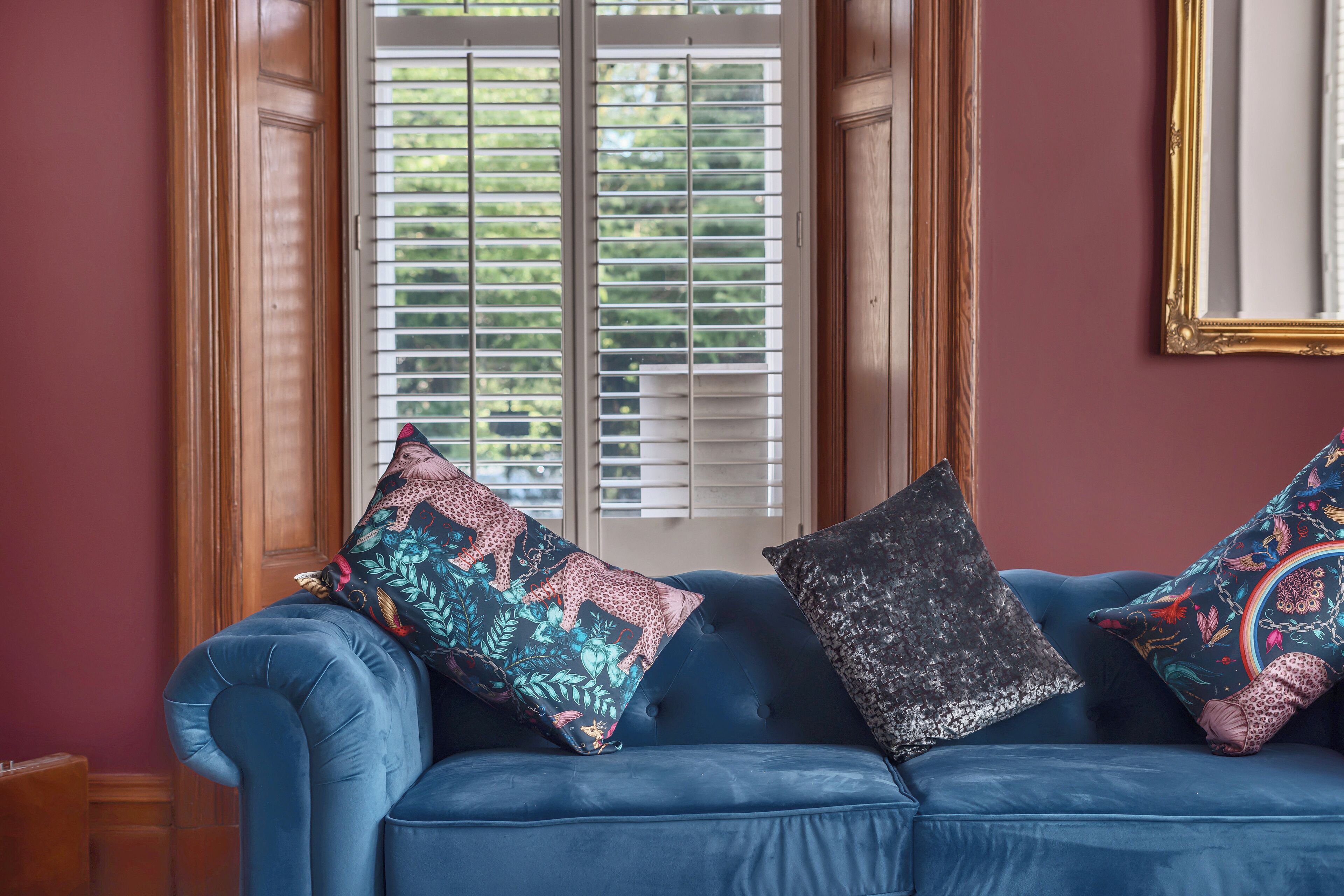 A blue sofa with patterned cushions in a room with wooden trim and a window with blinds.