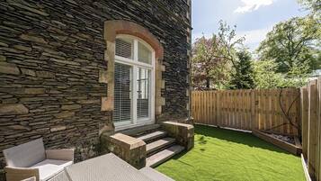 A stone building with a wooden deck, outdoor seating, and a well-maintained lawn.