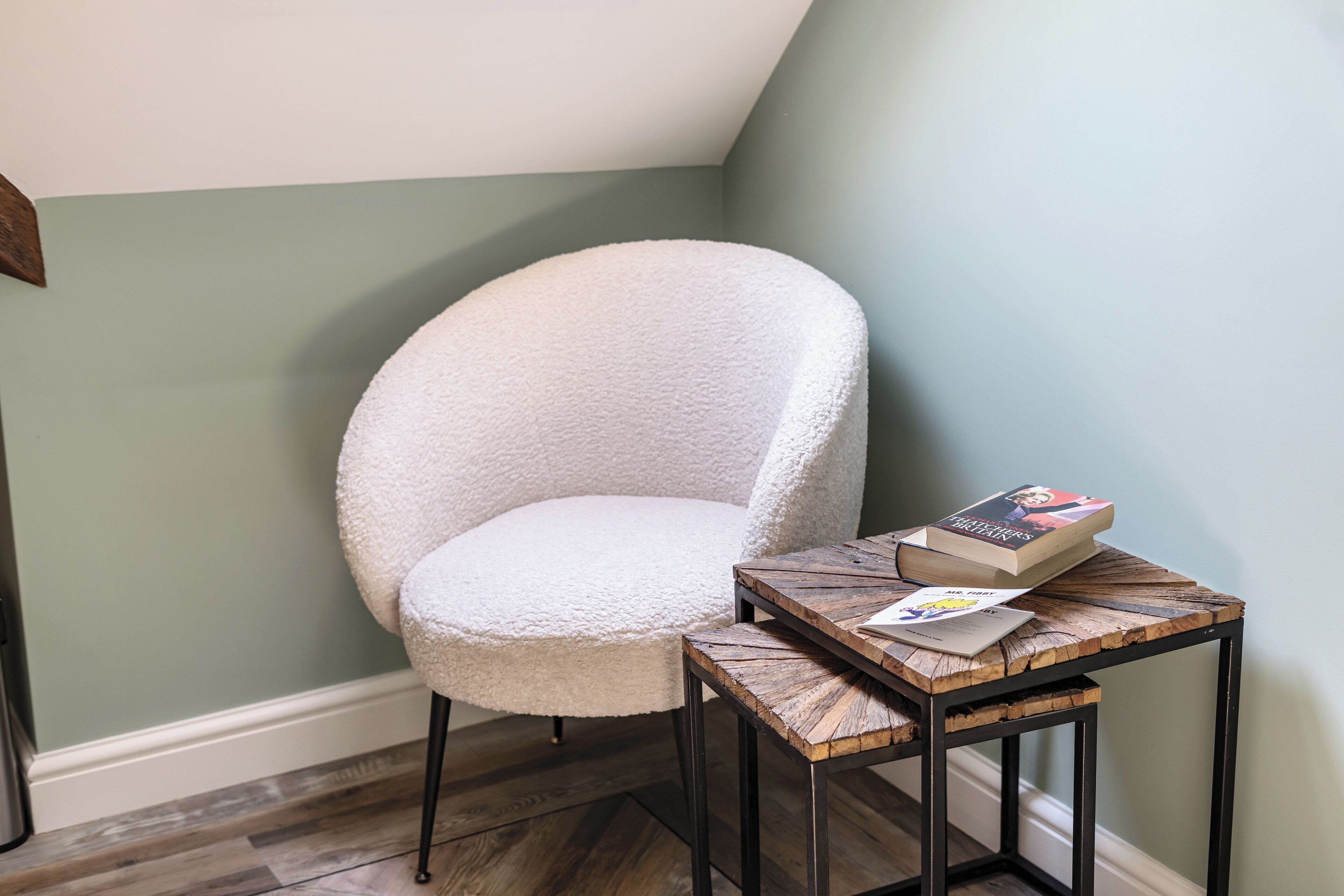 A white armchair next to a wooden side table with a book and a menu.