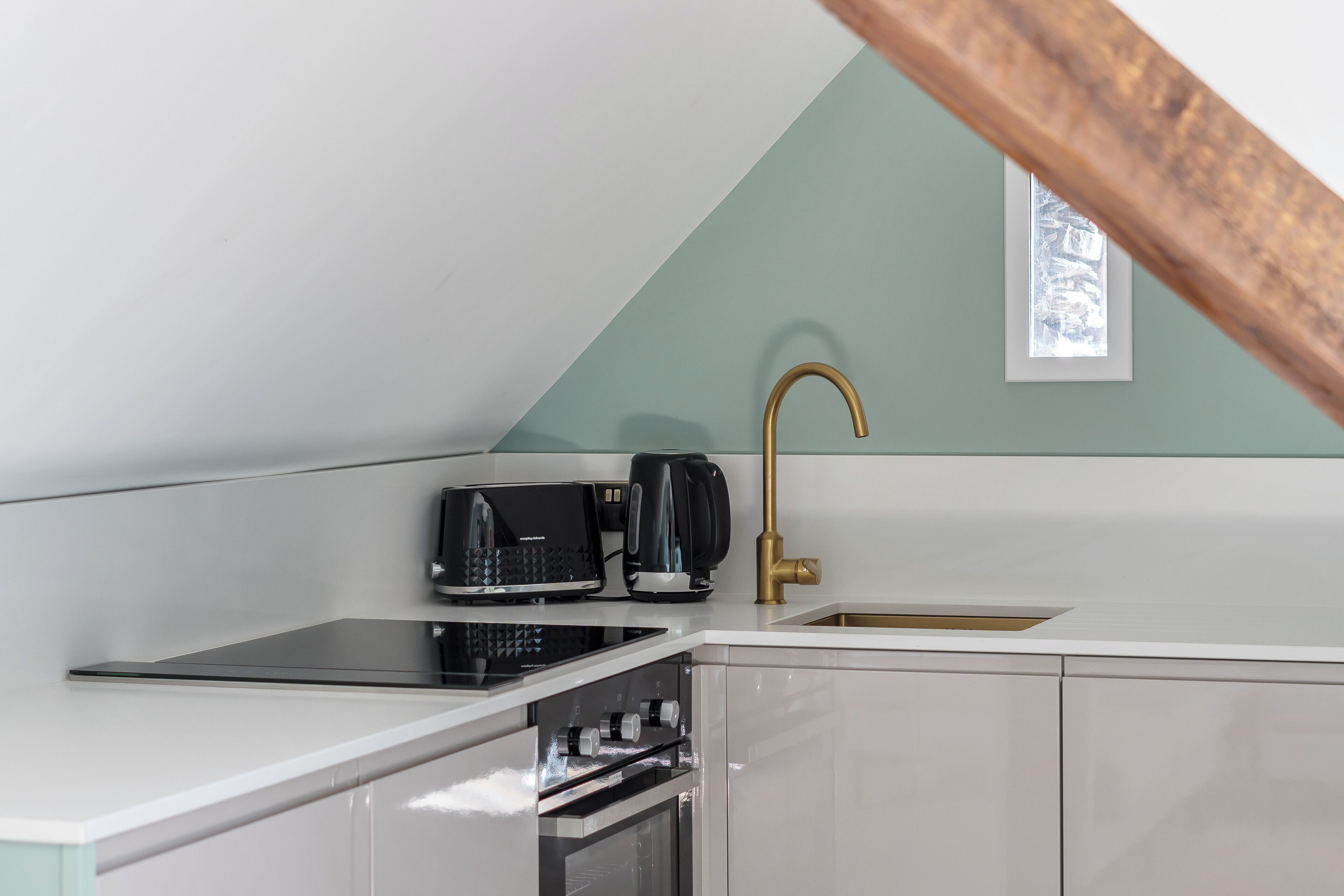 A kitchen with a white countertop, a black coffee maker, a gold faucet, and a window with a view.
