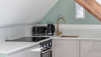 A kitchen with a white countertop, a black coffee maker, a gold faucet, and a window with a view.