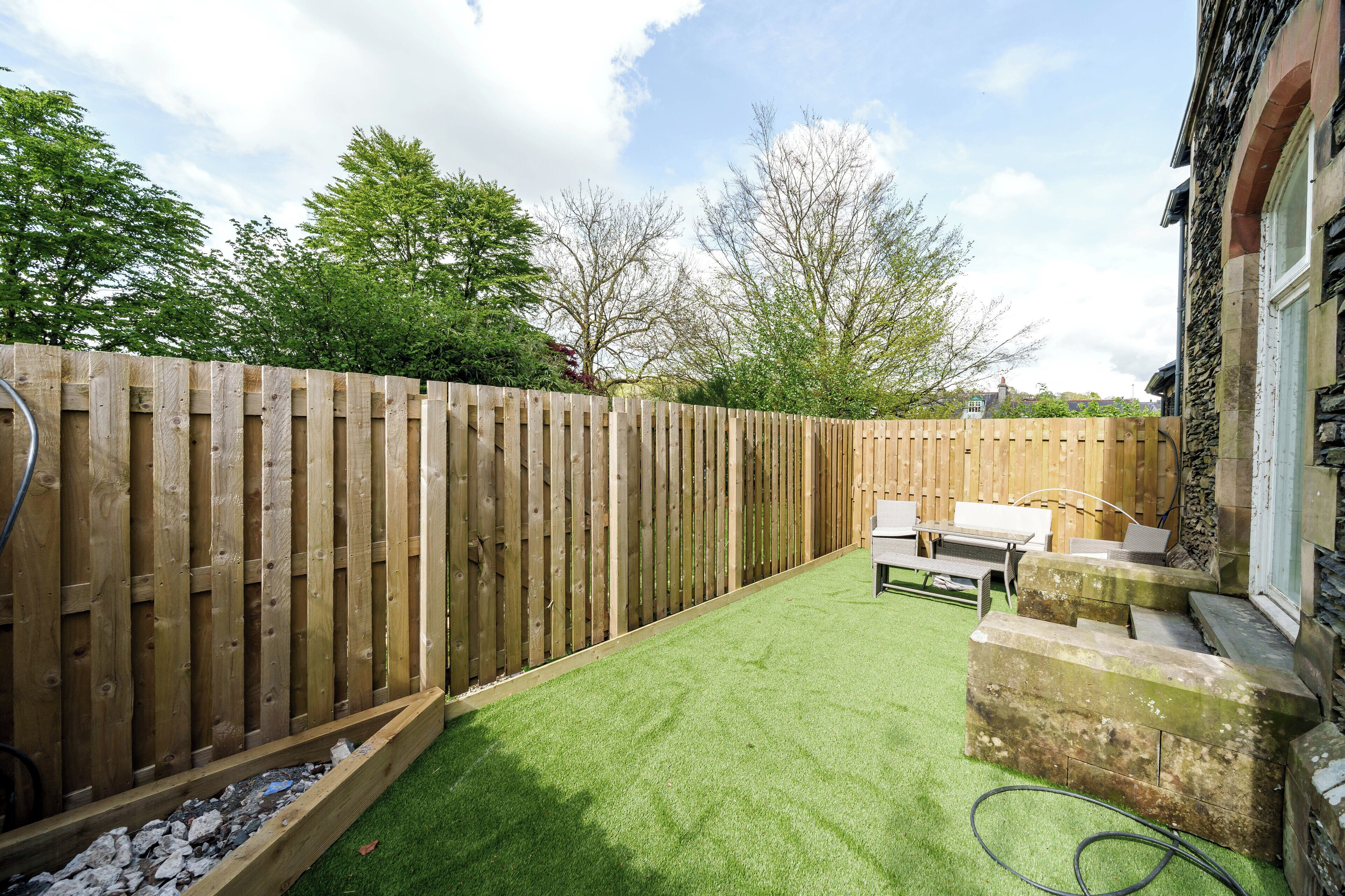 A backyard with a wooden fence, a grassy lawn, and a stone wall.