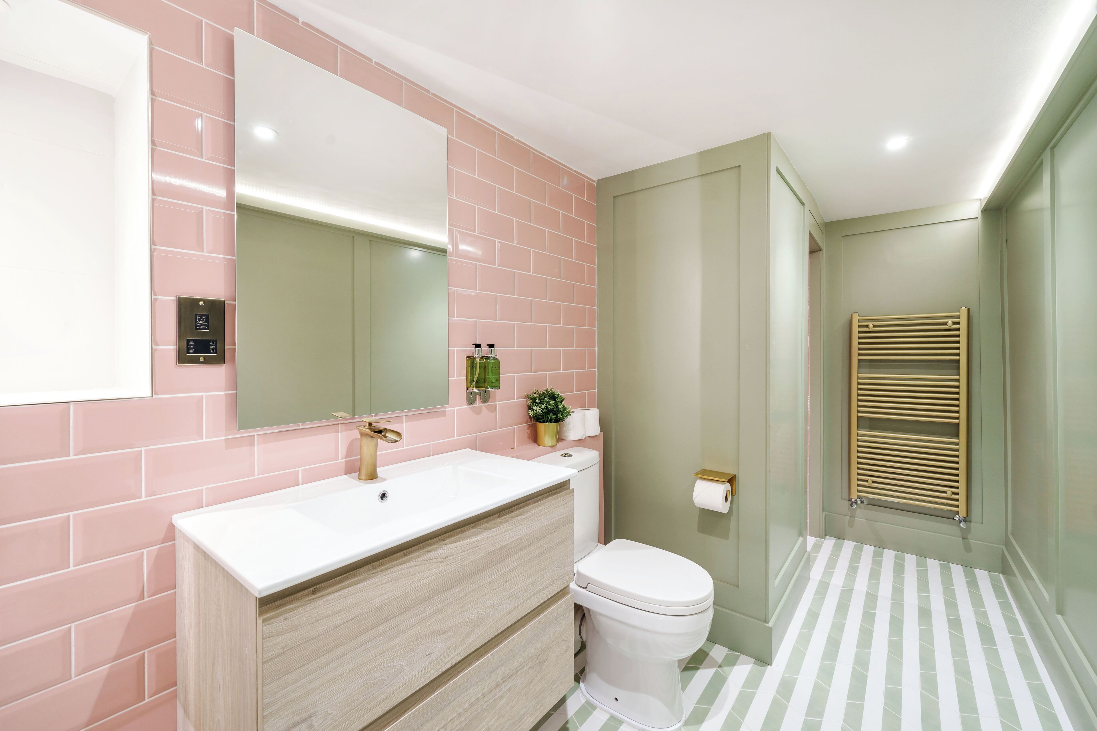 A bathroom with a pink-tiled wall, a white sink, a toilet, and a towel rack.
