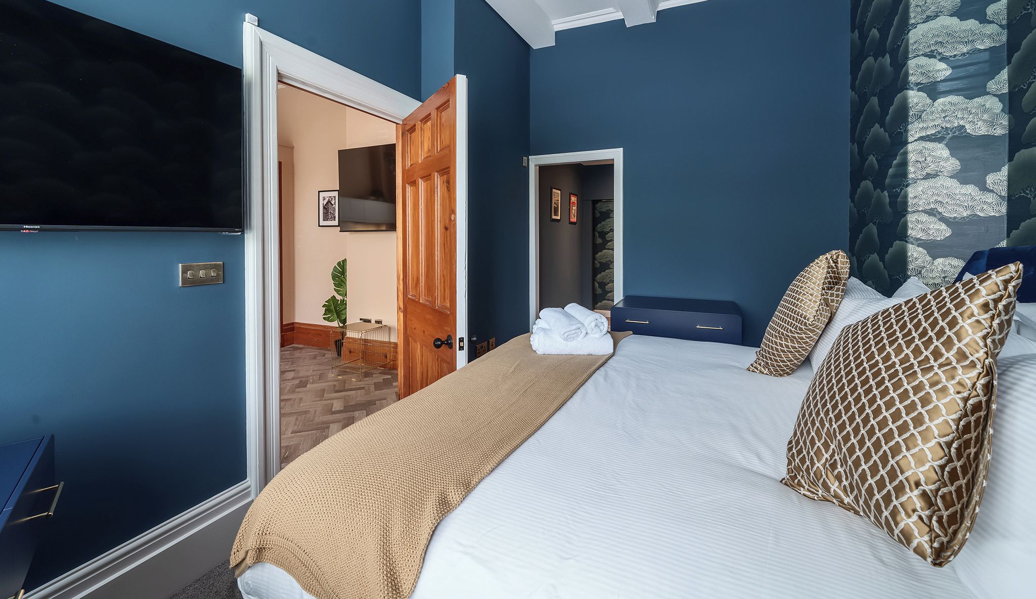 Una cama grande con televisión, una puerta de madera y una pared azul.