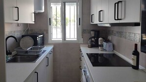 A modern kitchen with white cabinets, a built-in stove, a coffee maker, and a wine bottle. - House with 2 terraces and sea view. 2 Bedrooms, 500m from the Beach. (Puerto de Mazarrón)