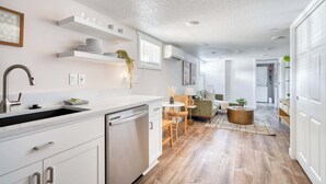 A modern kitchen with white cabinetry, a built-in dishwasher, and a dining area with a round table and chairs. - Vibrant Portland Getaway - Chic Flat (Portland)
