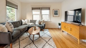 Una sala moderna con un sofá gris, una mesa de centro de madera y un televisor sobre un mueble de madera.