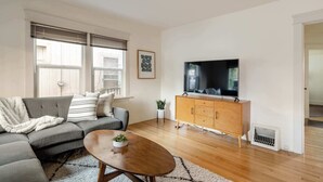 Una sala de estar moderna con un sofá modular, una mesa de centro de madera, un televisor sobre un mueble de madera y una pequeña planta.