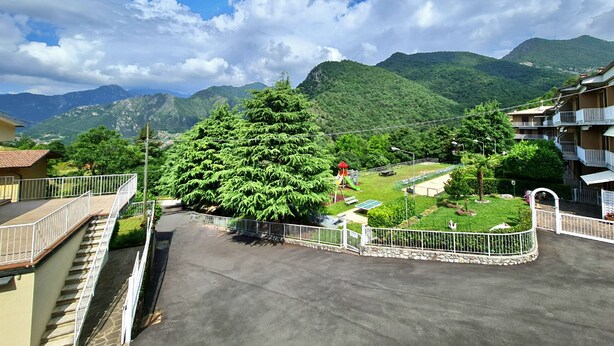 A residential area with a large green tree, a playground, and a view of mountains. - Casa Luana alla Glera (Tremosine)