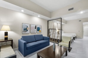 A hotel room with a blue sofa, a small table, a bed, and a decorative screen.