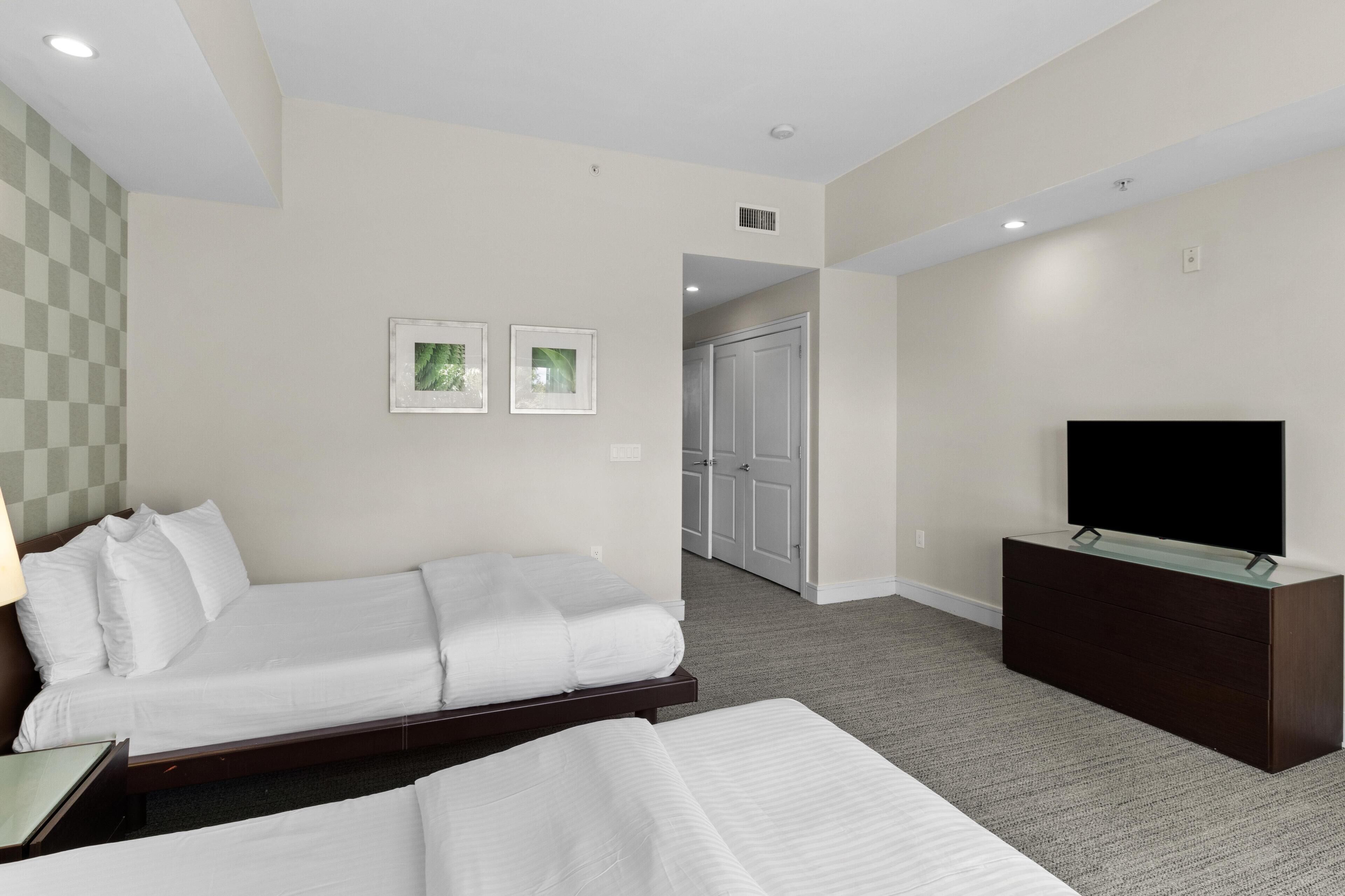 A hotel room with a bed, a TV on a dresser, and a door leading to another room.