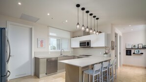 A modern kitchen with a central island, stainless steel appliances, pendant lighting, and a view of the outdoors. - Gorgeous 2BR Marina View Retreat (Río Hato)