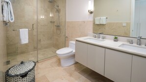 A modern bathroom with a glass-enclosed shower, a white toilet, and a large mirror above a double sink. - Gorgeous 2BR Marina View Retreat (Río Hato)