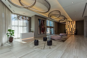 A spacious lobby with a modern design, featuring a large seating area, a reception desk, and a large window offering a view of the city.
