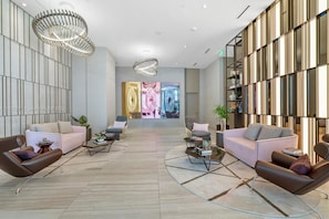 A spacious lobby with modern furnishings, including sofas and armchairs, a coffee table, and a large digital art display.