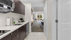 A modern kitchen with stainless steel appliances, a white countertop, and a view into the dining area. - Pool, Spa, Dining, Parking – Resort Style Studio (Miami)