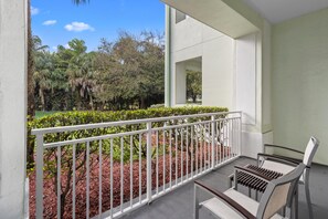 A balcony with a white railing, a bench, and a view of a landscaped garden with trees and shrubs. - Studio for 4, 1070 sq ft, Kitchen, Washer/Dryer (Miami)