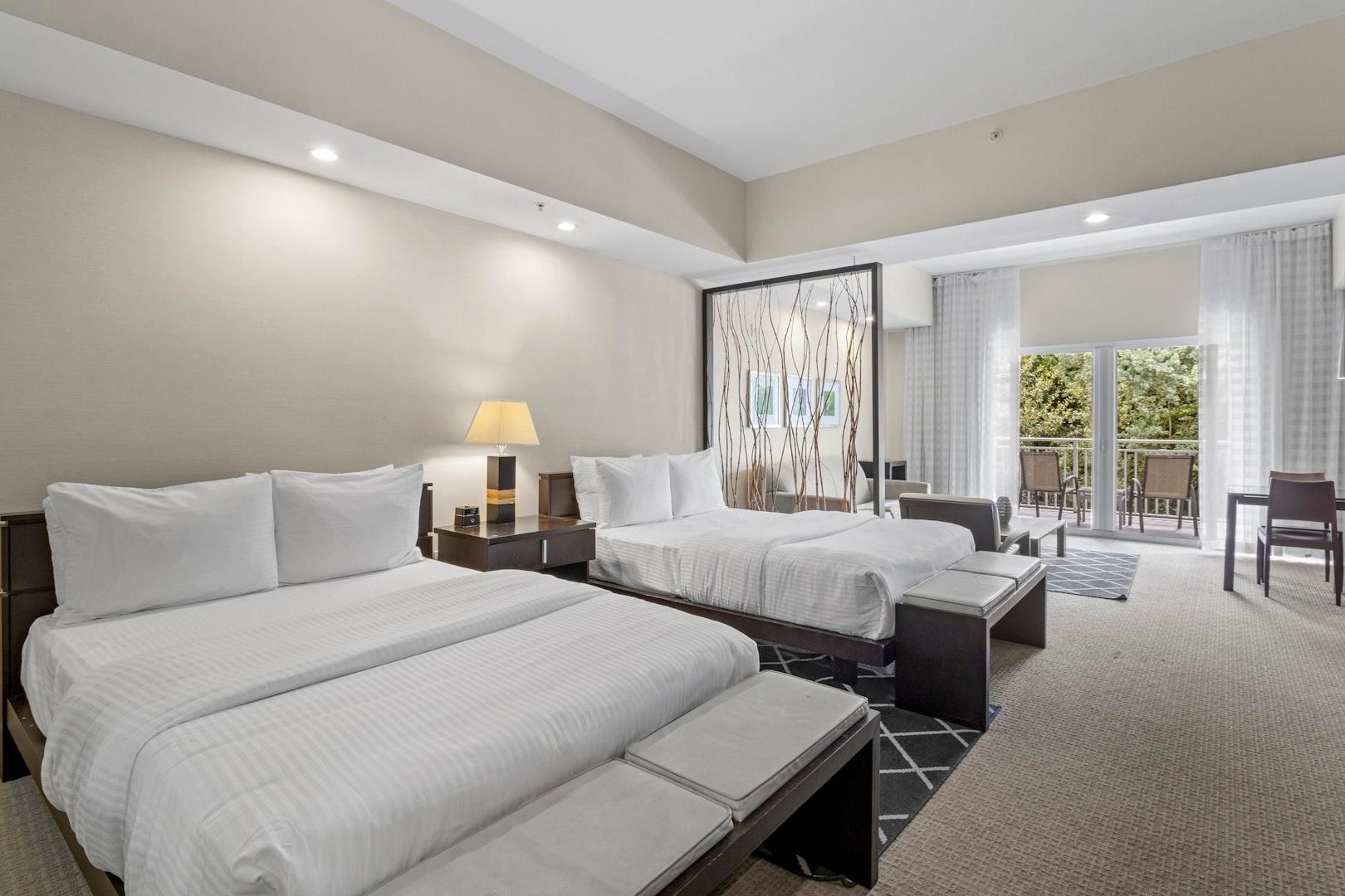 A hotel room with two beds, a desk, a chair, a balcony, and a large mirror.
