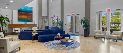A spacious lobby with a blue sofa, a round coffee table, and a large painting on the wall.