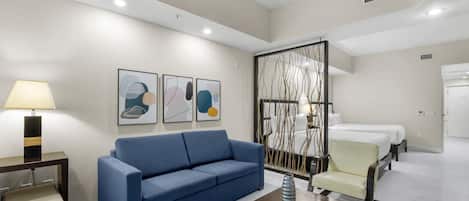 Una habitación de hotel con un sofá azul, una mesita, una cama y un separador decorativo.