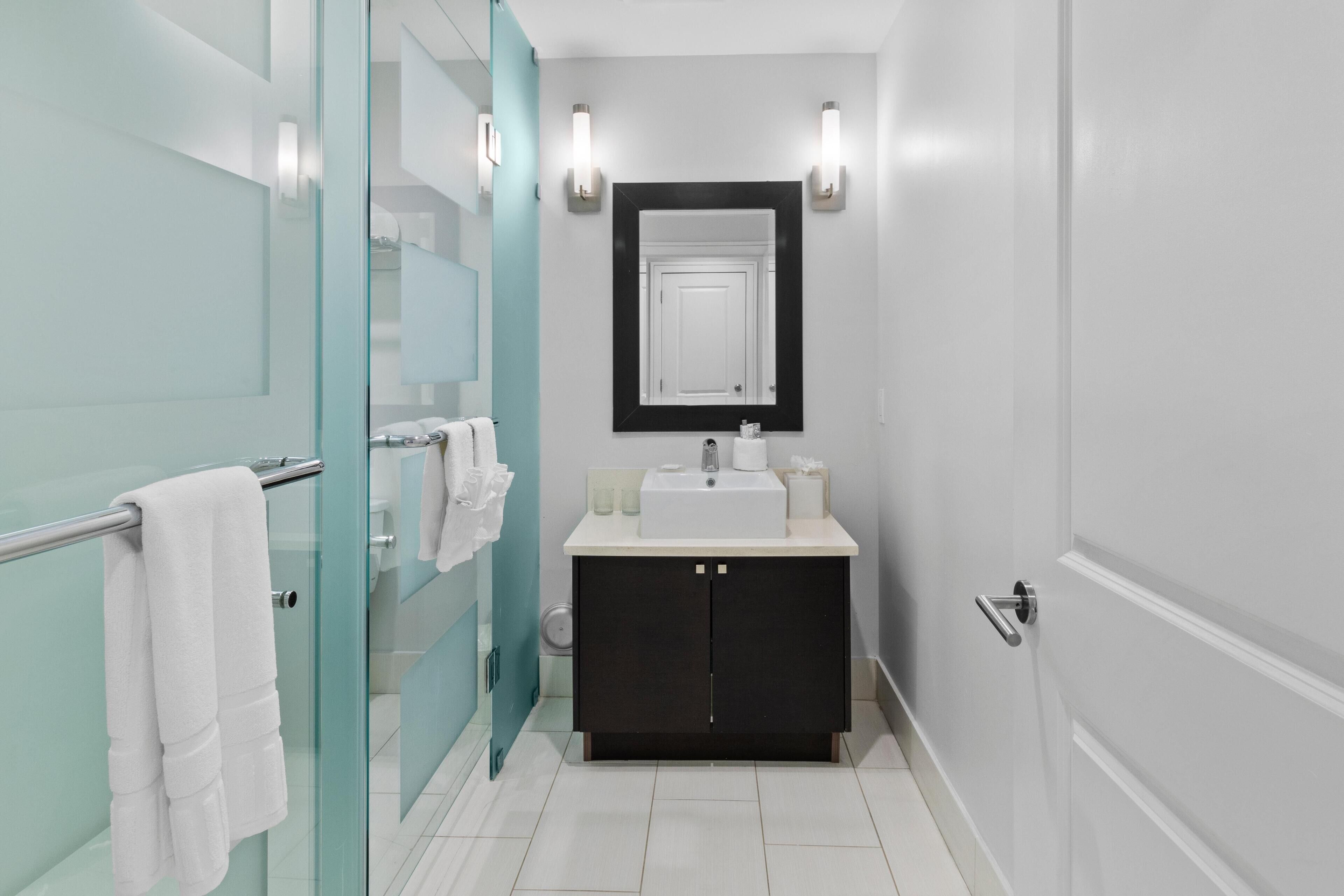 A modern bathroom with a glass shower enclosure, a white sink, and a black cabinet.