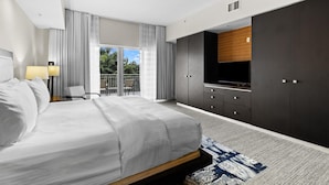A modern hotel room with a large bed, a TV, dark cabinets, and a balcony with a view. - Golf in Paradise – 3 Bedroom Townhouse in Doral (Miami)