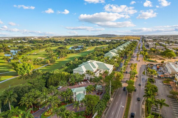 A golf course with a clubhouse, a road with vehicles, and a distant cityscape.