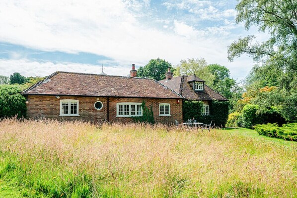A brick house with a tiled roof, surrounded by a grassy field and trees.