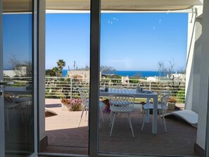 A balcony with a view of the sea, white furniture, and a stone wall.