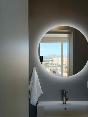 Un baño con un espejo redondo, un lavamanos blanco y una toalla colgada en la pared.