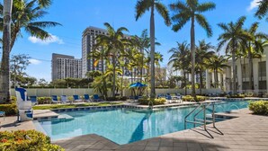 A swimming pool with lounge chairs and palm trees, surrounded by buildings. - Spacious 1,070 Sq Ft Studio with Kitchen (Miami)