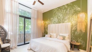 Une chambre avec un grand lit, une chaise, une petite table et une vue sur la verdure.