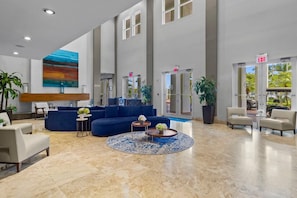 A spacious lobby with a blue sofa, a round coffee table, and a large painting on the wall. - King Suite with Kitchen, Washer/Dryer (Miami)