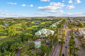 A golf course with a clubhouse, a road with vehicles, and a distant cityscape.