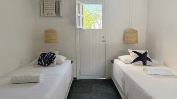 Una habitación pequeña y limpia, con dos camas, una puerta que da al exterior y una ventana con vistas a árboles.
