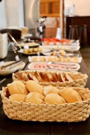 A buffet table with various food items and baskets of bread. -  Peixe Crew Centro (Búzios)