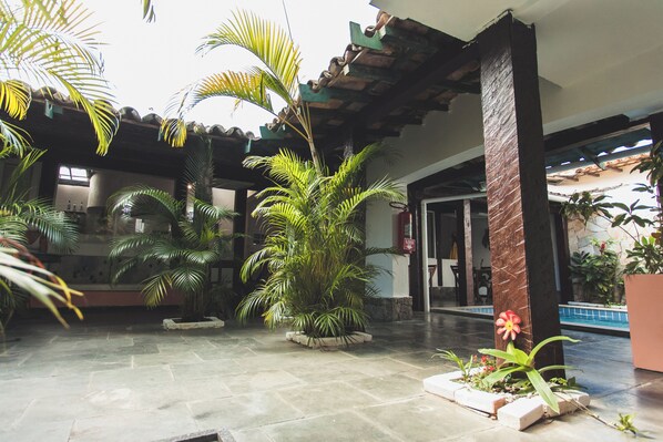 A spacious courtyard with a pool, surrounded by palm trees and potted plants. -  Peixe Crew Centro (Búzios)